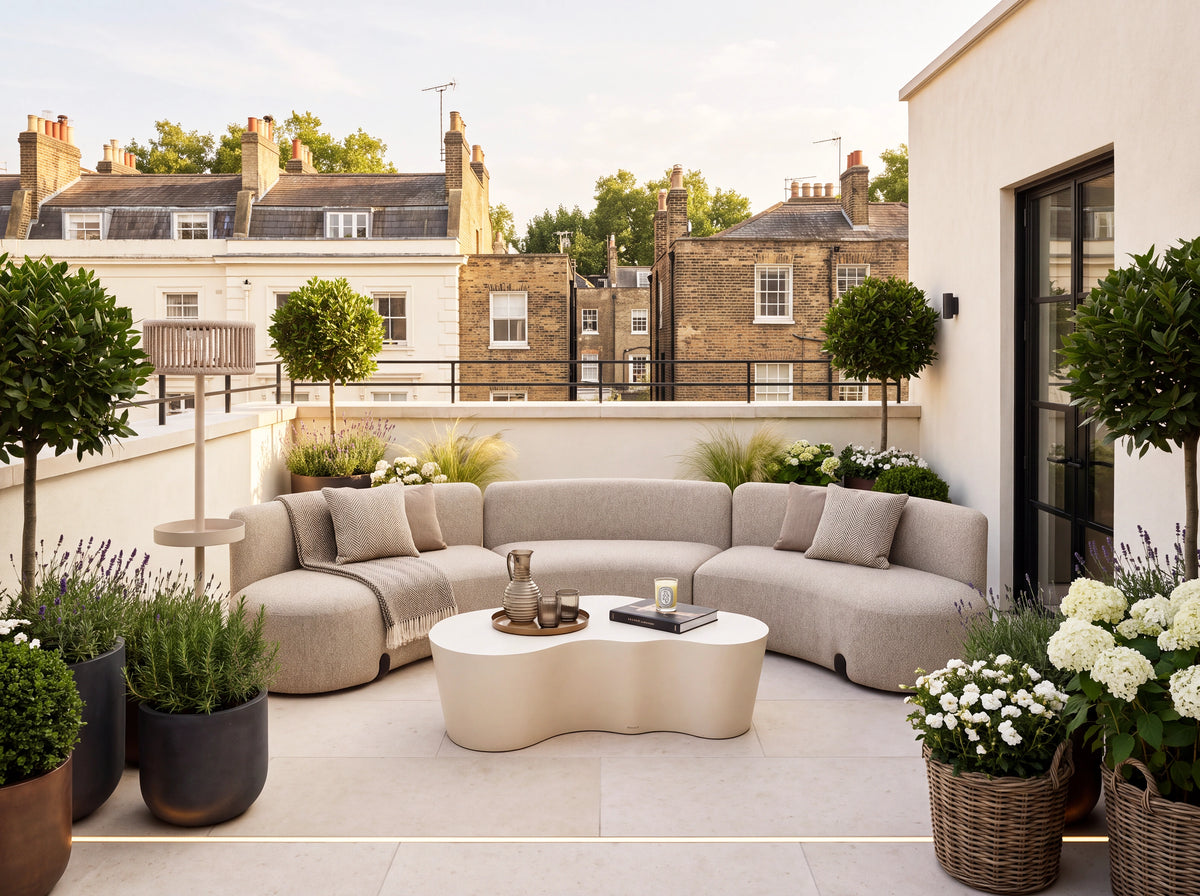 A modern curved outdoor sofa set on a rooftop terrace with a matching sculptural coffee table, surrounded by potted plants and overlooking city buildings in the background.